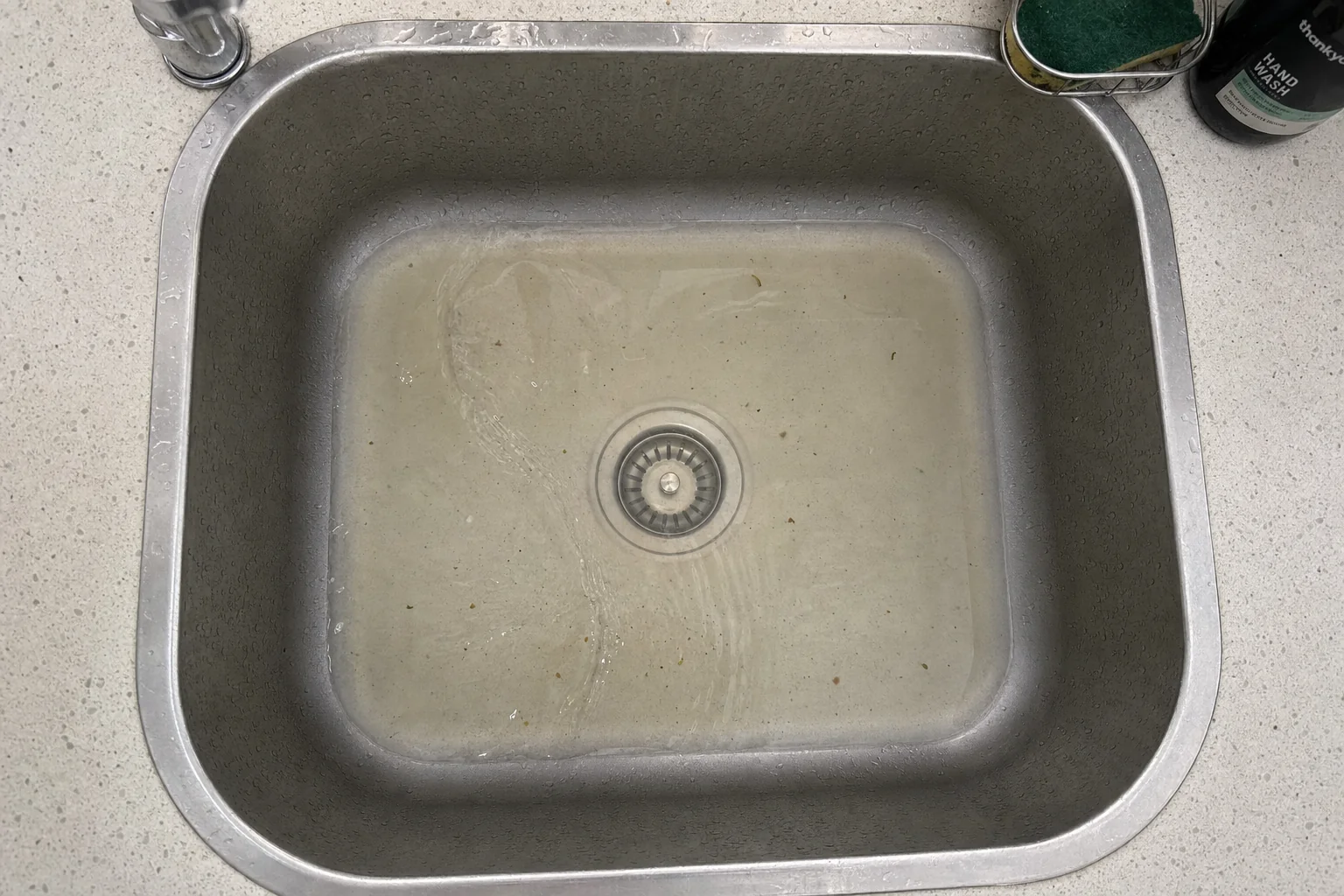 A kitchen sink holding a pool of slow-draining water, an early sign of a blocked drain